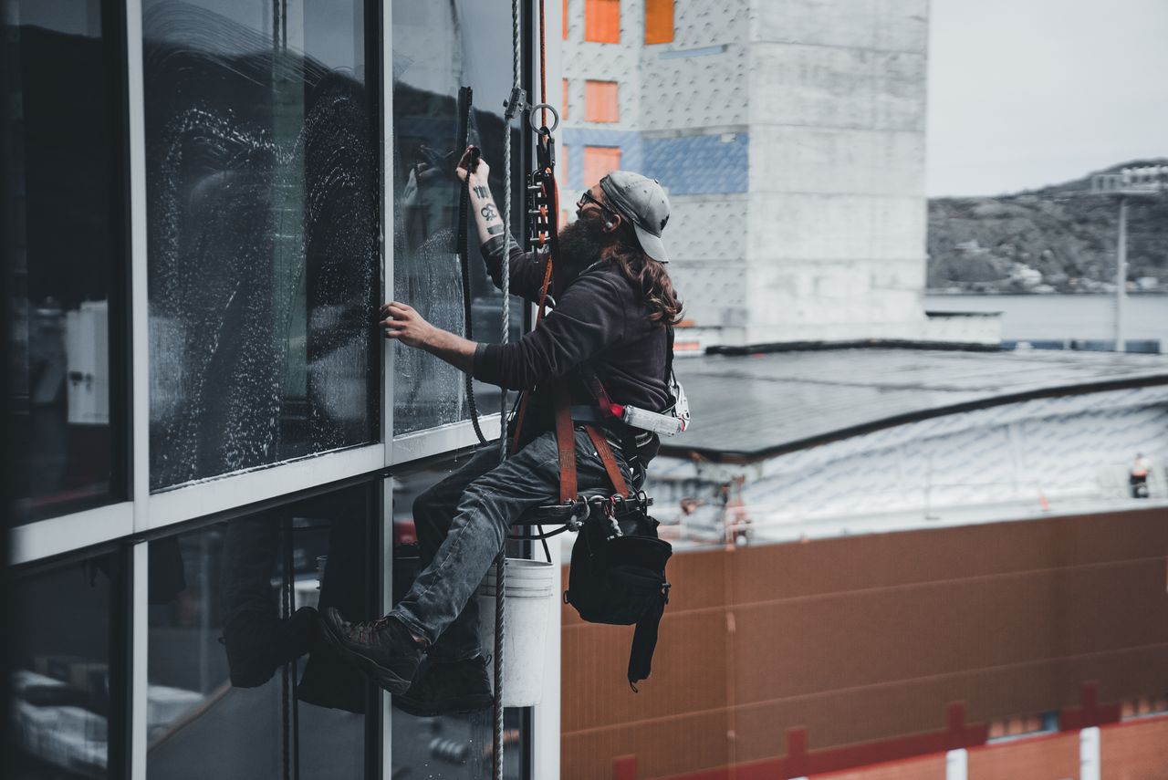 Un homme nettoyant les vitres d’un gratte-ciel avec un harnais, illustrant le travail en hauteur en milieu urbain.