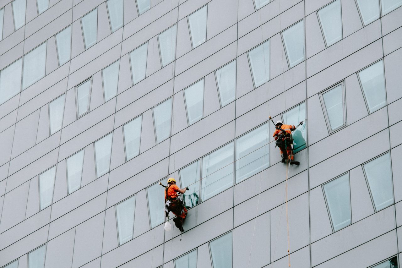Window cleaners working high above in protective equipment, washing the exterior of a skyscraper.